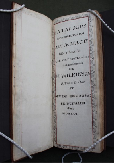 Tall, narrow book held open by book snakes. Book open to show hand drawn red and black in title page.