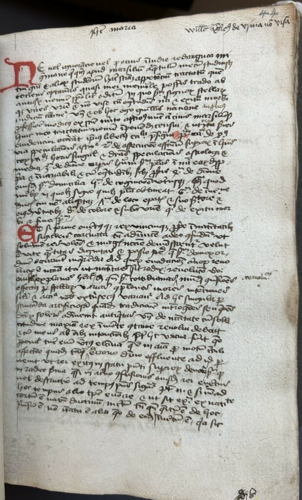 Book opening showing a handwritten page of Latin in black ink with two red initials.