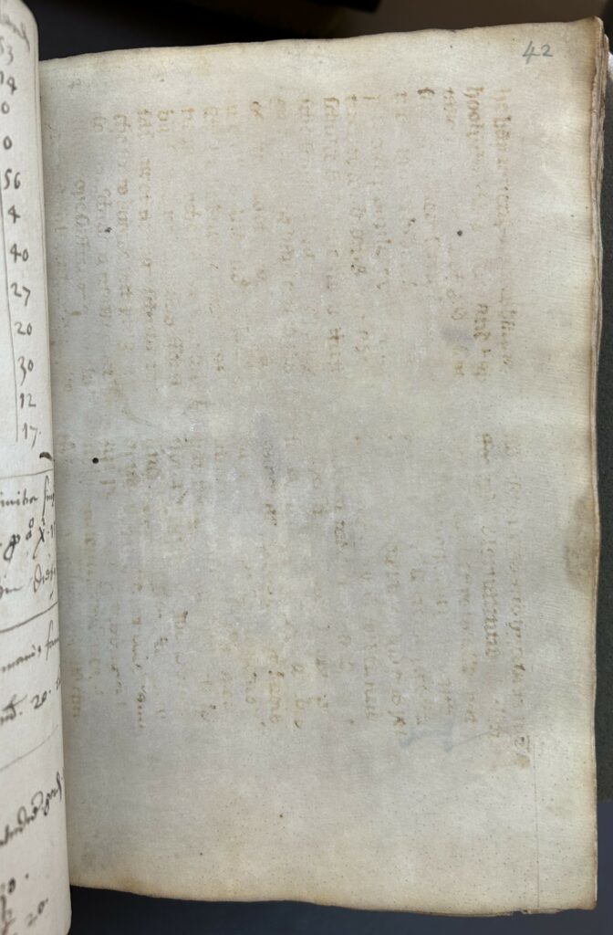 Book opening showing a page of parchment. The parchment has been cleaned but leaves some traces of previous handwriting in two columns. The traces of text are turned to a 90 degree angle, running vertically instead of horizonally. To the left of the image is part of the verso of the previous page with handwriting and numbers in black in.