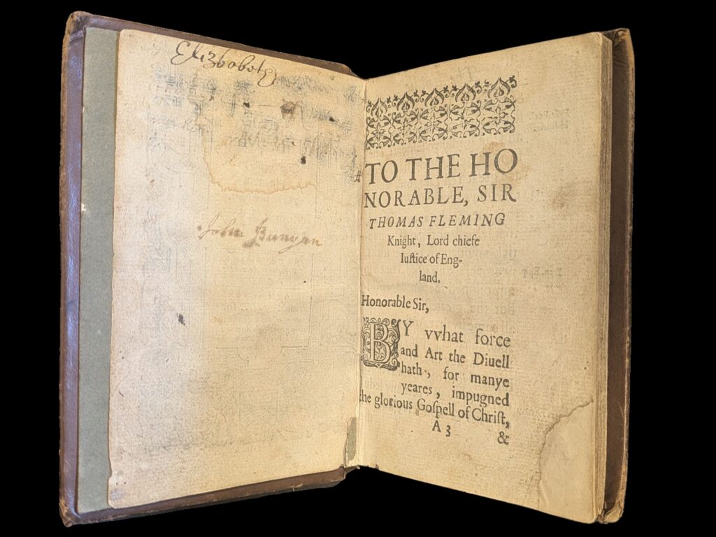 Left had pages has a signature 'Elizbobote' at the top of the page. In centre of the page is a signature 'John Bunyan' in ink that has leeched onto paper.  On the right page is the a printed dedication to 'The Honorable, Sir Thomas Fleming'