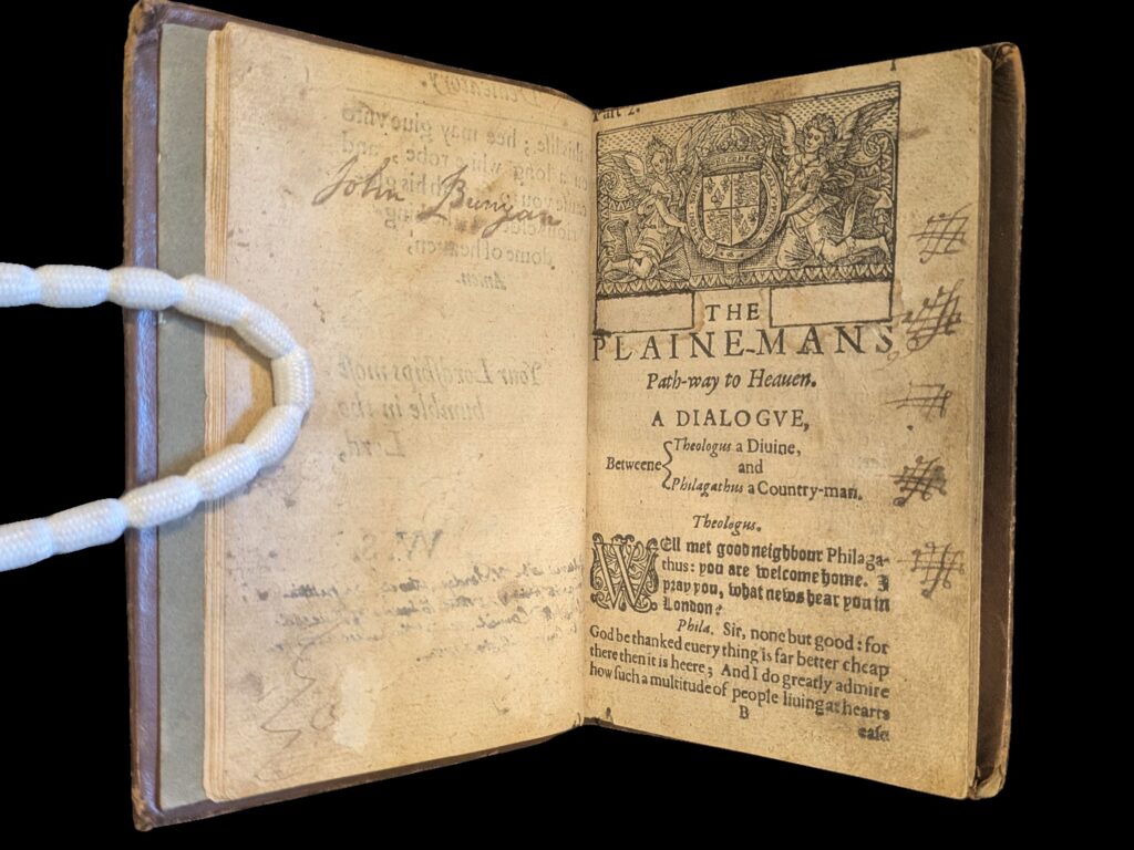 On the left page is a signature 'John Bunyan' in ink that leeched. On the right page is the first page of the main printed text with the royal crest above. There are ink doodles in the margin. 