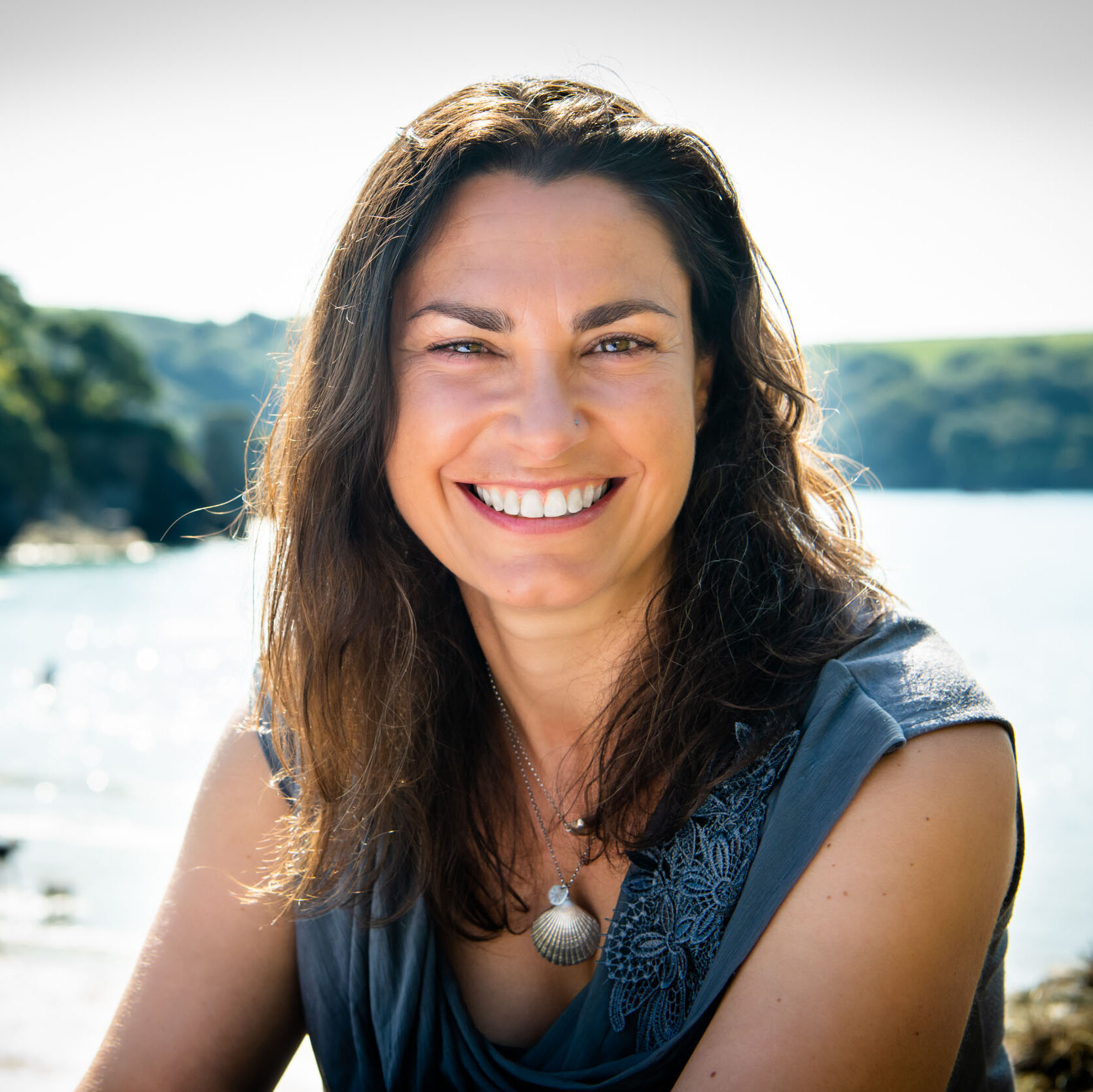 Portrait of Anna Turns smiling at the camera with a beach in the background.