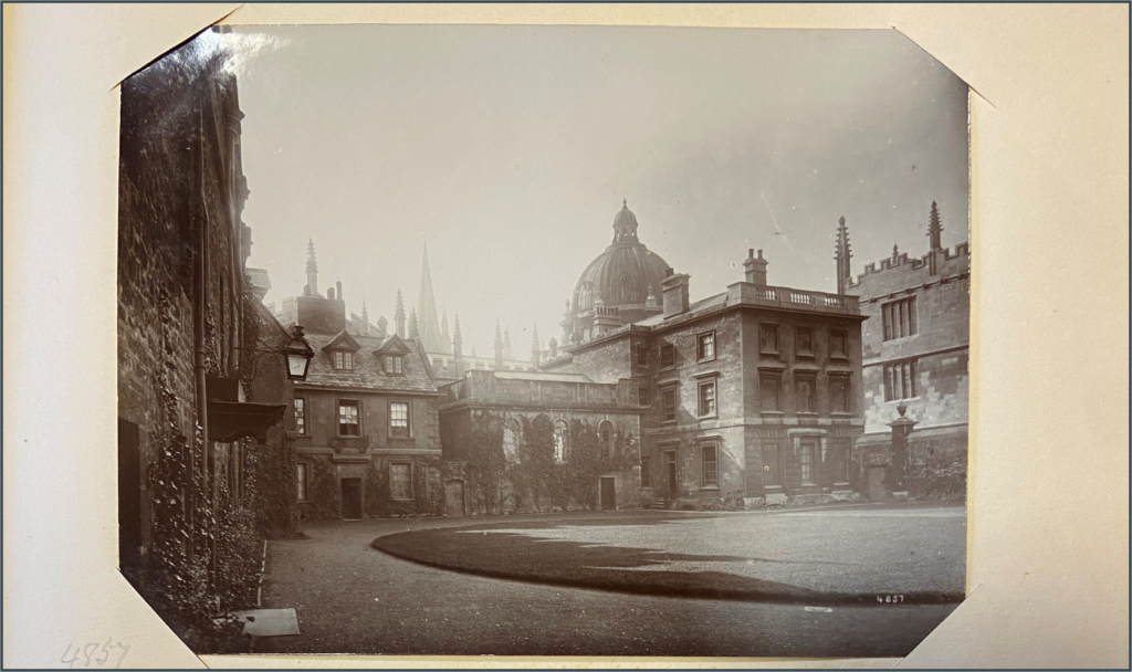Black and white picture of 19th century view of Old Buildings Quad, with rounded top of Radcliffe Camera visible behind stone buildings of quad.