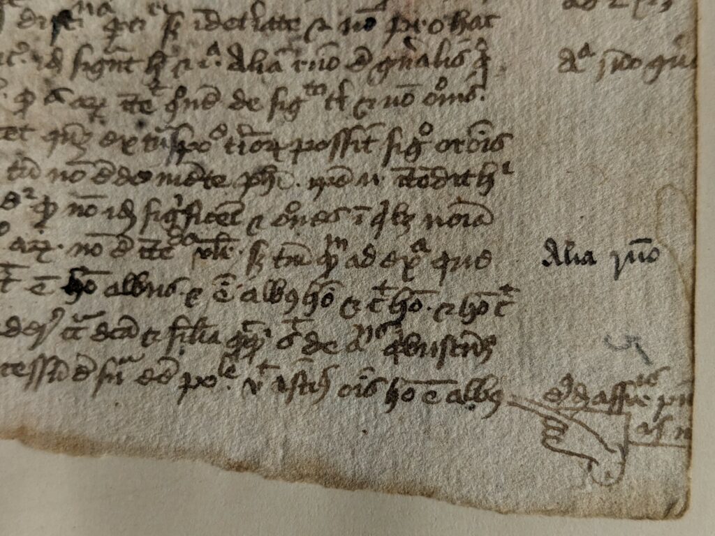 Close up of a manuscript page of text with a manicule in the bottom right corner pointing at the text.