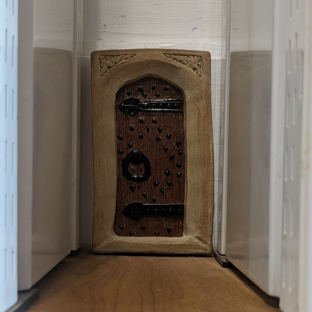 Close up of historic looking wooden door with black metal finishing. Door has a white wall around it and modern wooden vinyl on floor in front.