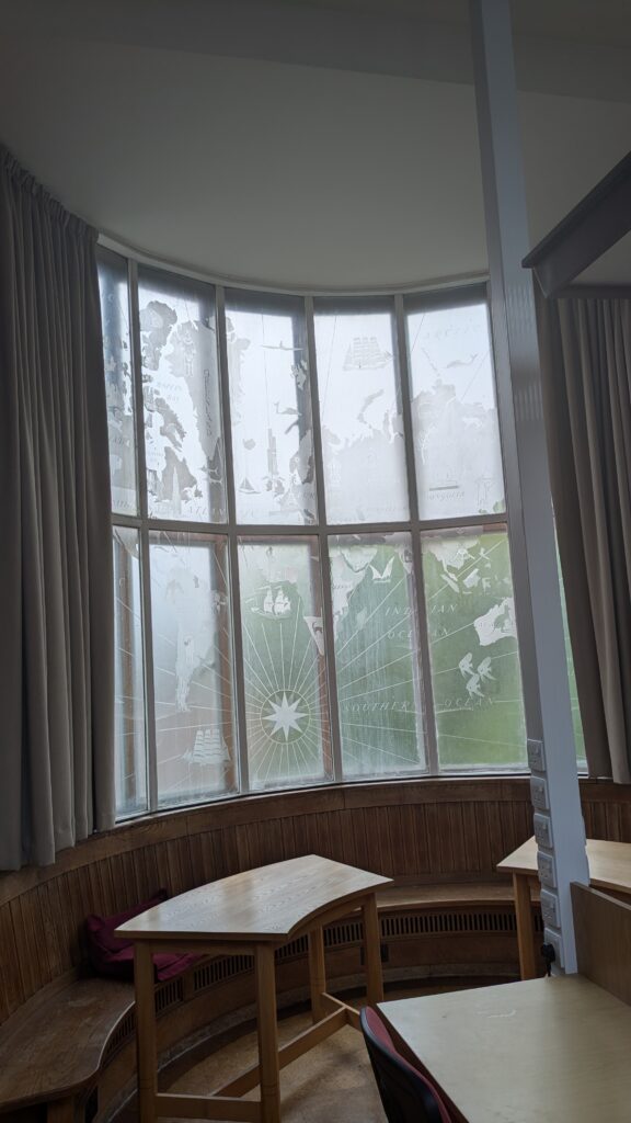 A curved window in Regent's park Library which has a map of the British Empire in frosted detail. There is a curved bench and two curved desks below it.