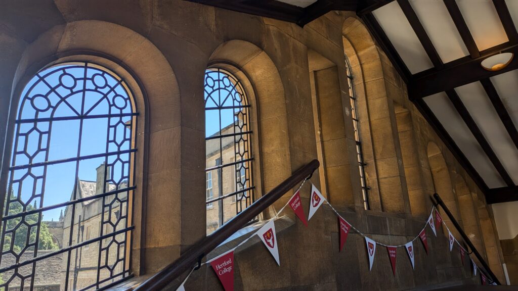 View of windows and ceiling of Hertford's bridge. Curved windows with decorative leadwork and a wood panelled ceiling. 