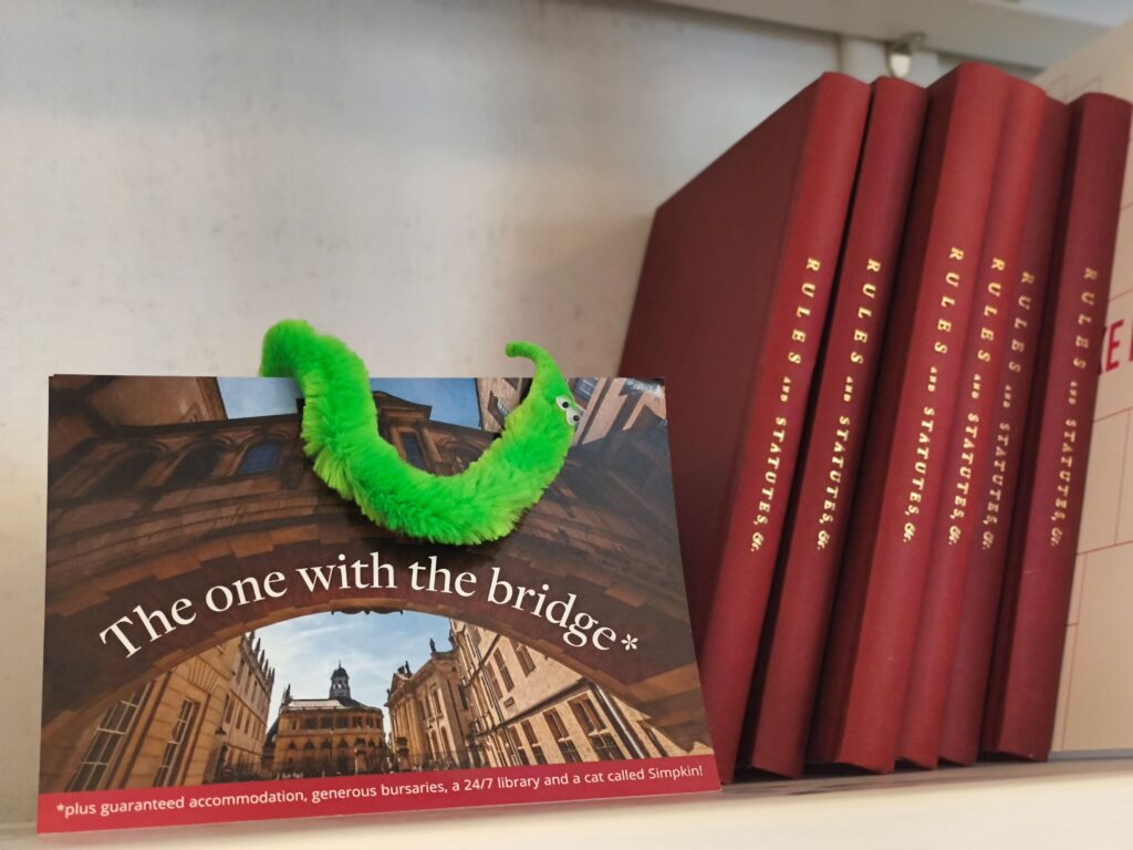Worm on a postcard of Hertford'd Bridge of Sighs next to red bound hardbacks with the gold title 'Rules and Statutes'