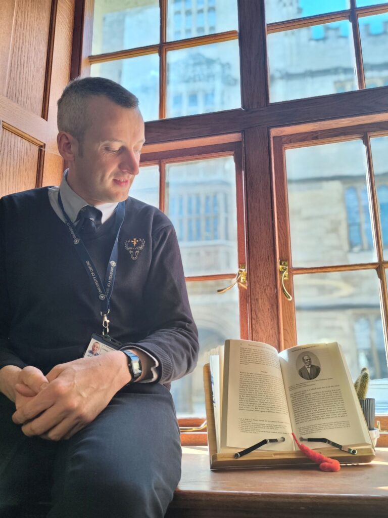 Man in Porter's uniform sat in window next to open book with worm also looking at book.