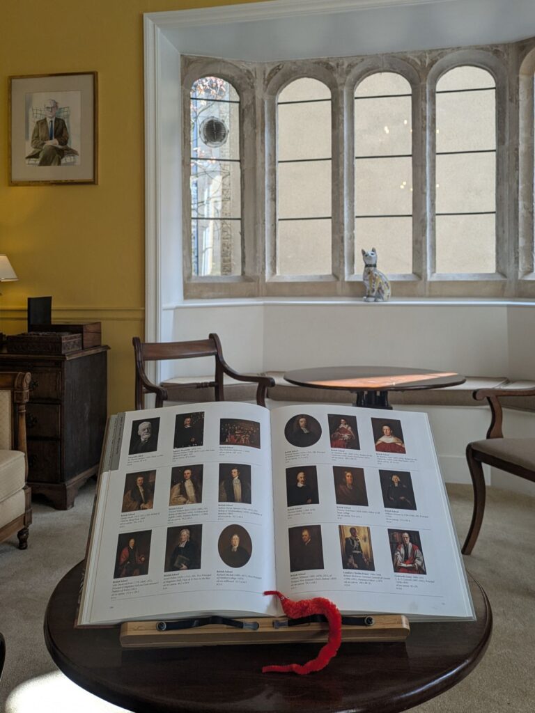 World with book of Hertford's oil paintings in a yellow room with wooden chairs and tables.