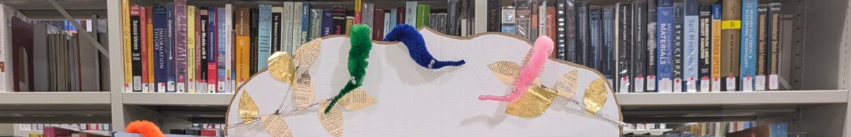 Worms draped over a cardboard frame in front of book shelves.